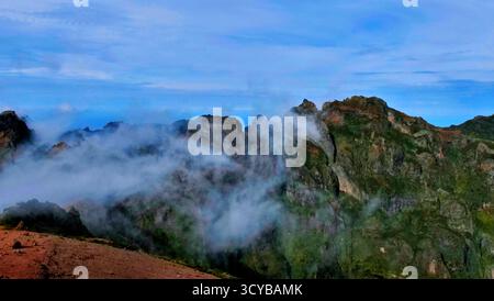 Neblige Berglandschaft mit dramatischen Klippen, Morgenlicht und rötlichen Felsen. Ätherische Wolken treiben durch grüne Täler. Perfekt für die Natur, Trav Stockfoto