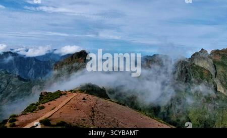 Neblige Berglandschaft mit dramatischen Klippen, Morgenlicht und rötlichen Felsen. Ätherische Wolken treiben durch grüne Täler. Perfekt für die Natur, Trav Stockfoto