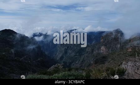 Neblige Berglandschaft mit dramatischen Klippen, Morgenlicht und rötlichen Felsen. Ätherische Wolken treiben durch grüne Täler. Perfekt für die Natur, Trav Stockfoto