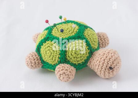Häkeln Sie Schildkröten-Kissen mit bunten Pins auf weißem Hintergrund Stockfoto