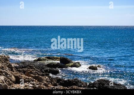 Ruhiger Blick auf die Küste mit felsigen Felsvorsprüngen und klarem blauem Wasser unter einem hellen Himmel Stockfoto