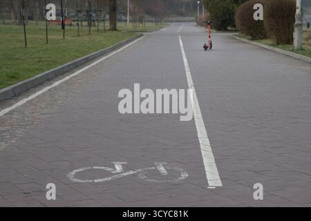 Städtischer Radweg mit weißen Markierungen und einem Elektroroller in der Ferne an einem bewölkten Tag. Stockfoto