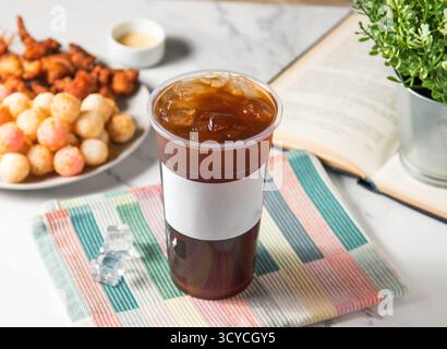 Eisschwarzer Tee serviert in Plastikglas mit Eiswürfel isoliert auf Serviette Seitenansicht von taiwan kaltem Getränk Stockfoto