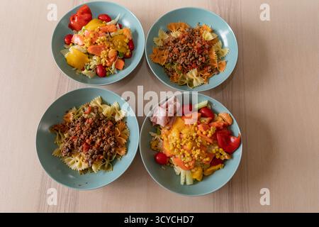 Hausgemachtes Mittagessen mit Pasta, frischem Gemüsesalat und Drachenfrüchten, die in türkisfarbenen Schüsseln auf Holztisch angeordnet sind. Stockfoto