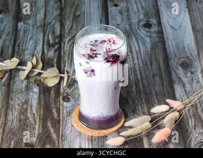Ice Blueberry Latte mit cremiger Milch und einem lebendigen Heidelbeerstrudel. Das Getränk wird in einem hohen Glas mit Eiswürfeln serviert und bietet seitlichen Blick auf das Refreshin Stockfoto