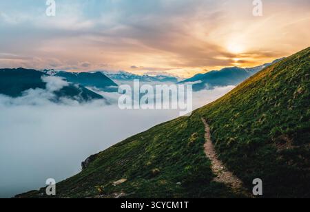 Atemberaubender Panoramablick auf einen gewundenen Bergpfad, der über eine dicke Wolkenschicht hinaufsteigt und von einem strahlenden goldenen Sonnenuntergang beleuchtet wird Stockfoto