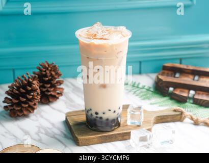 Ice Pearl Milk Tea mit Eiswürfel in hohem Glas serviert auf einem Holzbrett, Seitenansicht auf taiwan kaltes Getränk Stockfoto