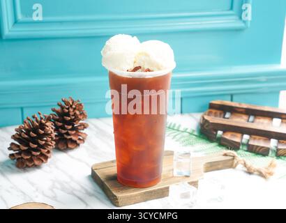 Schwarzer Eistee mit zwei Schaufeln Vanilleeis und Eiswürfel in hohem Glas serviert auf einem Holzbrett, Seitenansicht des kalten Getränks taiwan Stockfoto