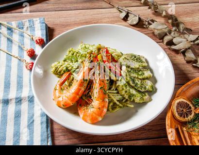 Meeresfrüchte-Pesto-Pasta mit Garnelen und gegrilltem Fisch belegt grüne Pesto-Sauce serviert auf einem Teller isoliert auf Holztisch Seitenansicht von taiwanischen Speisen Stockfoto