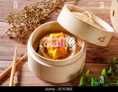 Krabbenroe Siu Mai gedämpfte Dumpling in Bambus Steamer mit Essstäbchen isoliert auf Holztisch Seitenansicht von Dim Sum taiwan Essen Stockfoto