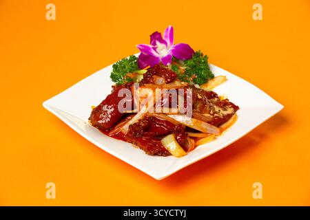 Chinesisches Rinderfilet mit Zwiebeln serviert auf Teller isoliert auf orangem Hintergrund Seitenansicht von hongkong Essen Stockfoto
