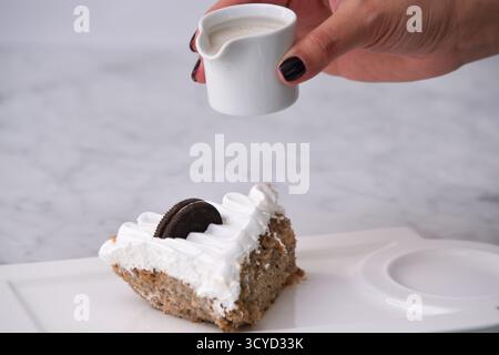 Oreo Cream Cake Slice mit zerkleinerten Schokoladen-Sandwichkeksen, gebacken mit Schlagsahne und tropfender Milchsauce, serviert auf einem Teller, der auf bac isoliert ist Stockfoto