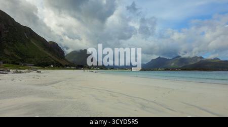 Weiße Sandstrände erstrecken sich entlang der Küste, während sanfte Wellen an der Küste entlang schlängeln. Üppige grüne Berge ragen im Hintergrund unter bewölktem Himmel auf. Ramberg, Rambe Stockfoto