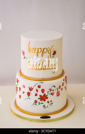 Dekorierte zweistufige Floral Happy Birthday Torte mit glattem weißem Milchglas, Seitenansicht der feierlichen Torte, perfekt für Geburtstage Stockfoto