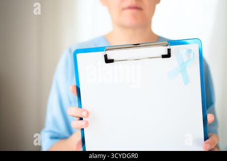 Nahaufnahme einer Ärztin in medizinischer Uniform mit Klemmbrett mit leerem Papier und blauem Band Symbol für Prostatakrebs Bewusstsein und Prävention in November Gesundheitskampagne Stockfoto