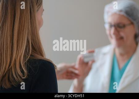 Von hinten eine Krankenschwester in weißen Uniformen Händen Medizin zu einer Patientin in einer Krankenhausumgebung. Hebt die professionelle Gesundheitsversorgung, Behandlungspläne und die Patientenbetreuung hervor. Stockfoto