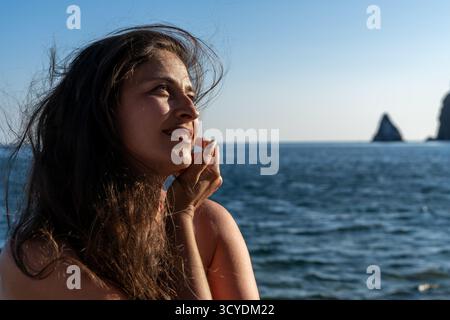 Frau, Meer, Sonnenuntergang. Schöne Frau lächelt und blickt auf das offene Meer während der goldenen Stunde mit Kopierraum Stockfoto