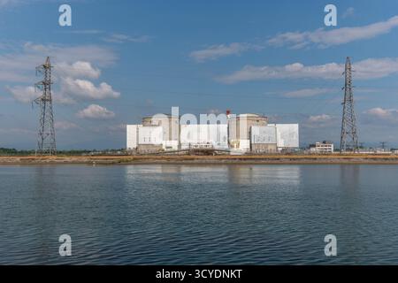 Eine große industrielle Atomanlage liegt an einer ruhigen Uferpromenade. Zwei hohe zylindrische Strukturen dominieren die Skyline, wobei Stromleitungen verlaufen Stockfoto