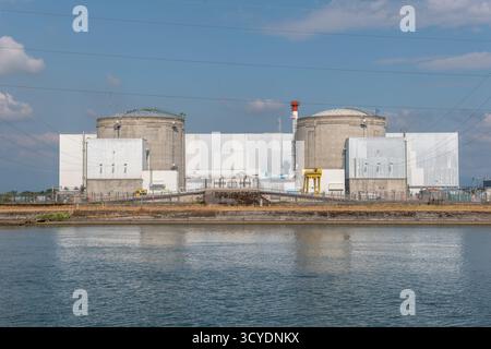 Eine große industrielle Atomanlage liegt an einer ruhigen Uferpromenade. Zwei hohe zylindrische Strukturen dominieren die Skyline, wobei Stromleitungen verlaufen Stockfoto