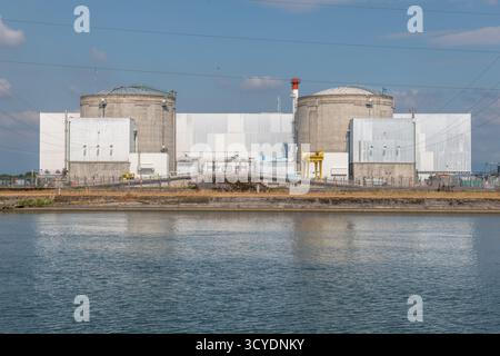 Eine große industrielle Atomanlage liegt an einer ruhigen Uferpromenade. Zwei hohe zylindrische Strukturen dominieren die Skyline, wobei Stromleitungen verlaufen Stockfoto