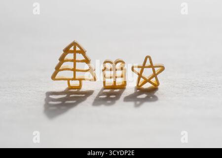 Pasta in Form eines Weihnachtsbaums, Geschenke, Miniatur-Weihnachtsmann und Stern, auf hellem Hintergrund. Ideal für Projekte im Zusammenhang mit Feiertagen, Kochen Stockfoto