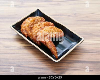 Glasierte Chicken Wings, bestreut mit Sesamsamen, serviert in schwarzer Schale, isoliert auf dem Tisch, Seitenansicht eines japanischen Cousins Stockfoto