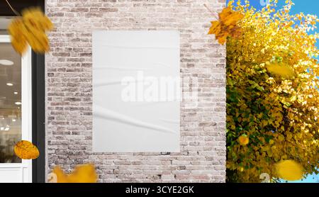 Weißes Poster an Ziegelwänden mit gelben Blättern in Bewegung, ideal für Mockups für Außenwerbung und saisonale Kampagnenbilder Stockfoto