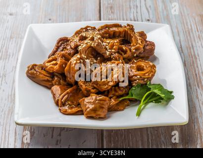 Geschmorte Schweinedärme mit einer reichhaltigen Sauce, bestreut mit Sesamsamen und frischem Koriander serviert auf einem Teller auf Holztisch Nahaufnahme von Hong Kon Stockfoto