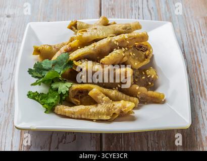 Geschmorte Hähnchenfüße mit herzhafter Soße, Sesamsamen und Koriander serviert auf einem Teller auf dem Holztisch Nahaufnahme von Hong Kong Essen Stockfoto