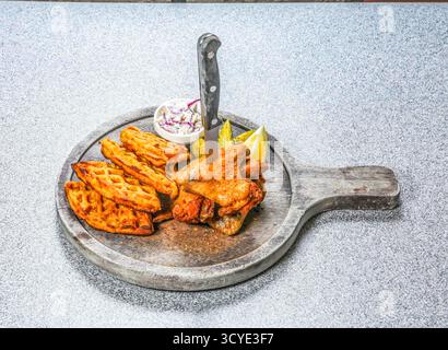 Chicken Wings and Waffles beinhaltet ein Messer, das in das Essen eine Seite von Krautsalat gesteckt wurde, und Zitronenscheiben, die auf einem Holzbrett serviert werden, Seitenansicht von hongkong-Speisen Stockfoto