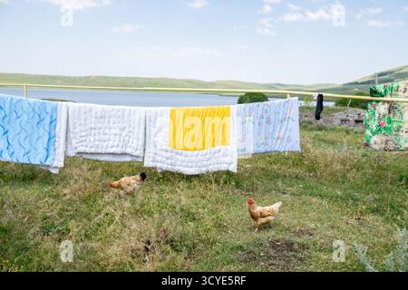 Hühner, die unter einer Wäscheleine mit Trockendecken und Decken in der Nähe des Ufers des Paravani Sees laufen. Paravani Lake, Javakheti, Georgia. 18. Juli 2020 Stockfoto