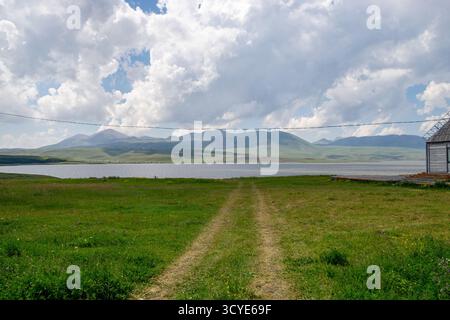 Weite Steppenlandschaft mit grünen Feldern, fernen Bergen und einem kleinen Dorf, das im Hintergrund zu sehen ist. Javakheti, Georgien. 18. Juli 2020. Stockfoto