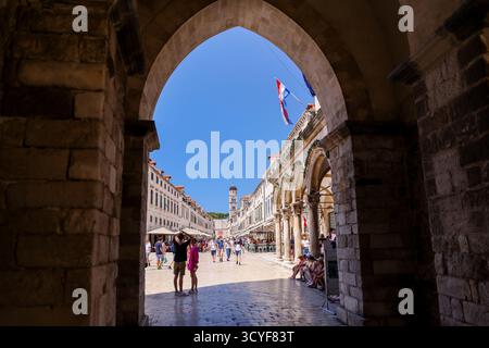 Menschen, die entlang der Stradun Street spazieren gehen, durch einen bogenförmigen Eingang in der Altstadt von Dubrovnik, Kroatien – Juli 2022. Stockfoto