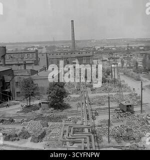 Dieses archivierte Schwarzweißfoto aus den 1970er Jahren bietet einen Panoramablick auf die Slawjansk Armature-Isolator Plant (AIZ) in Sloviansk, UdSSR. Der riesige Industriehof dient als riesiges Freiluftlager, das mit Tausenden von fertigen Isolatoren auf Paletten gefüllt ist. Durch den Hof verläuft ein Netz von Hochleitungen und Eisenbahngleisen. Ein mobiler Kran und ein hoher Schornstein sind in dieser Szene sowjetischer Industrieskala zu sehen Stockfoto
