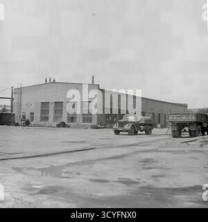 Dieses Archivfoto aus den 1970er Jahren zeigt einen großen Hof in der Slawjansk Armature and Insulator Factory (AIF) in Slowiansk, ukrainische SSR. Ein Tankwagen, wahrscheinlich ein GAZ-Modell, steht vor einem langen Backsteingebäude. Ein weiterer Lkw ist rechts sichtbar, und der Boden ist nass mit Pfützen. Dieses Bild zeigt die Transportlogistik und das Arbeitsumfeld eines großen sowjetischen Industriewerks, eine Momentaufnahme des friedlichen Donbass. Stockfoto