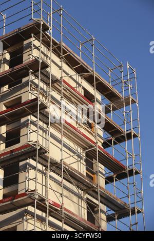 Ein Gebäude im Bau mit Gerüsten an der Seite. Das Gerüst ist rot und weiß. Das Gebäude ist hoch und hat viele Fenster Stockfoto