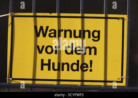 Ein gelbes Schild mit schwarzer Aufschrift, auf dem Warning: Vor dem Hunde! Hängt an einem Zaun Stockfoto