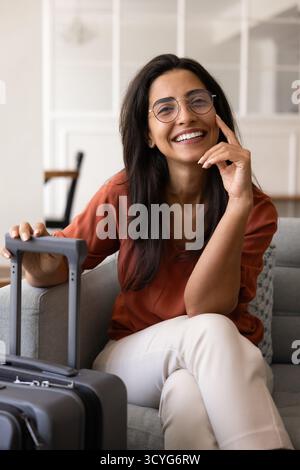 Fröhlich, schöne hispanische Reisetägerin in Brille, die für Porträt posiert Stockfoto