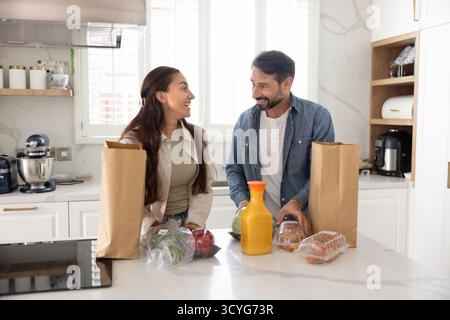 Glückliches verheiratetes Paar, das große Einkaufstaschen mit Lebensmitteln auspackt Stockfoto