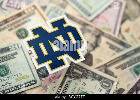 KIEW, UKRAINE - 23. FEBRUAR 2025 Notre Dame Fighting Irish Basketball Team Badge liegt auf einer großen Menge von US-Dollar-Scheinen Stockfoto