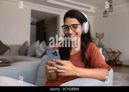 Fröhliche junge hispanische Frau, die Musik vom Smartphone hört Stockfoto