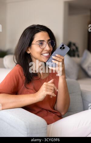 Positive engagierte junge Lateinfrau in Brille, die eine Sprachnachricht spricht Stockfoto