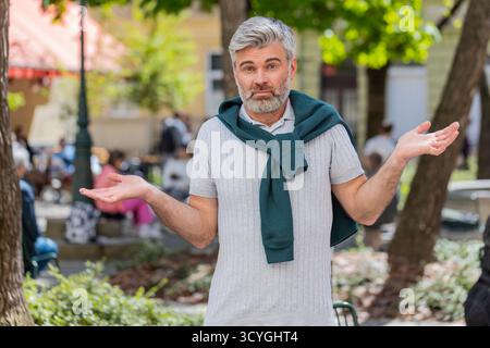 Ich weiß nicht, was ich sagen soll. Verwirrter reifer Mann, der sich über zweideutige Fragen peinlich fühlt, Zweifel hat, keine Ahnung hat, im Freien ahnungslos unsicher ist. Kaukasischer Erwachsener, der in der Stadtstraße steht Stockfoto