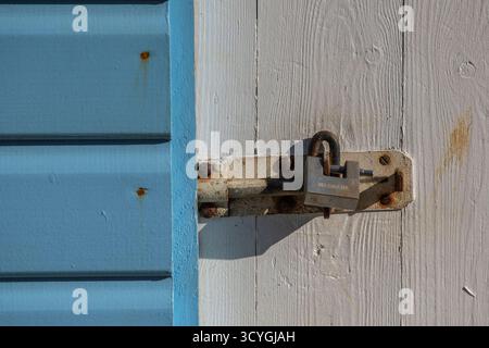 Rostiger Haspe und Klammerschloss auf einer alten, schäbigen, schicken, verwitterten Strandhütte am Meer. Sicheres Schloss auf hölzerner Strandhütte oder Chalethütte. Stockfoto