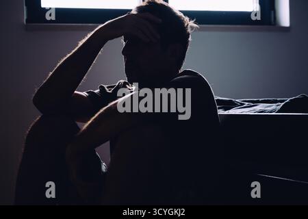 Silhouetted reifer Mann sitzend hoffnungslos und depressiv auf Schlafzimmerboden, mentale Gesundheit und Einsamkeit Konzept. Selektiver Fokus. Stockfoto