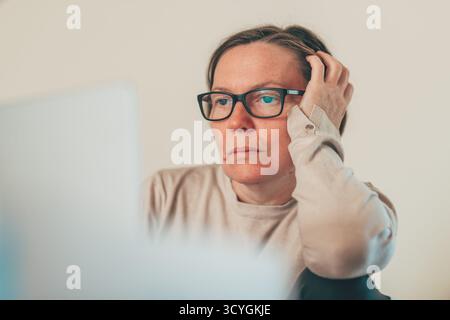 Reife Erwachsene Frau in Freizeitkleidung, gestresst und frustriert, während sie zu Hause am Laptop arbeitet. Selektiver Fokus. Stockfoto