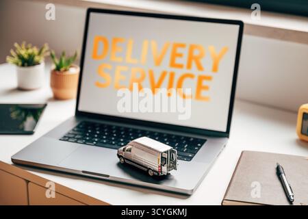 Laptop-Computer mit „Delivery Service“-Text mit Miniatur-Van-Modell auf der Tastatur, symbolisiert Logistik, Versand und E-Commerce-Lieferung Stockfoto