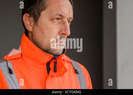 Fokussierter Bauingenieur in orangefarbener Sicherheitsjacke, der auf der Baustelle steht und Führungsqualitäten, Verantwortlichkeit und Engagement in modernen infras repräsentiert Stockfoto
