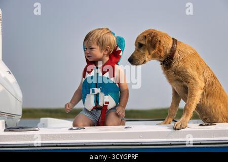 Ein Kind mit Schwimmweste, während er mit seinem Hund auf einem Boot sitzt Stockfoto