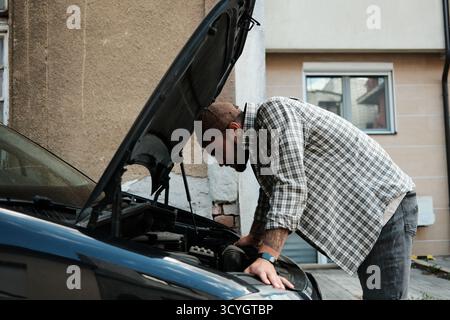 Junger Mann, der den Motor auf der Stadtstraße überprüft. Konzept der Reparatur, Wartung und Verantwortung. Stockfoto